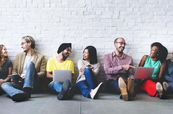 Various people sitting on the floor talking and holding laptops.